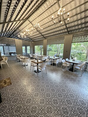 An indoor dining area with tables and chairs, a patterned floor, and a ceiling with a grid-like structure and hanging lights. - Olive Resorts & Villas (Kurai)