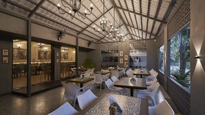 A restaurant with patterned flooring, white chairs, and tables, featuring a ceiling with chandeliers and large windows with a view of trees. - Olive Resorts & Villas (Kurai)