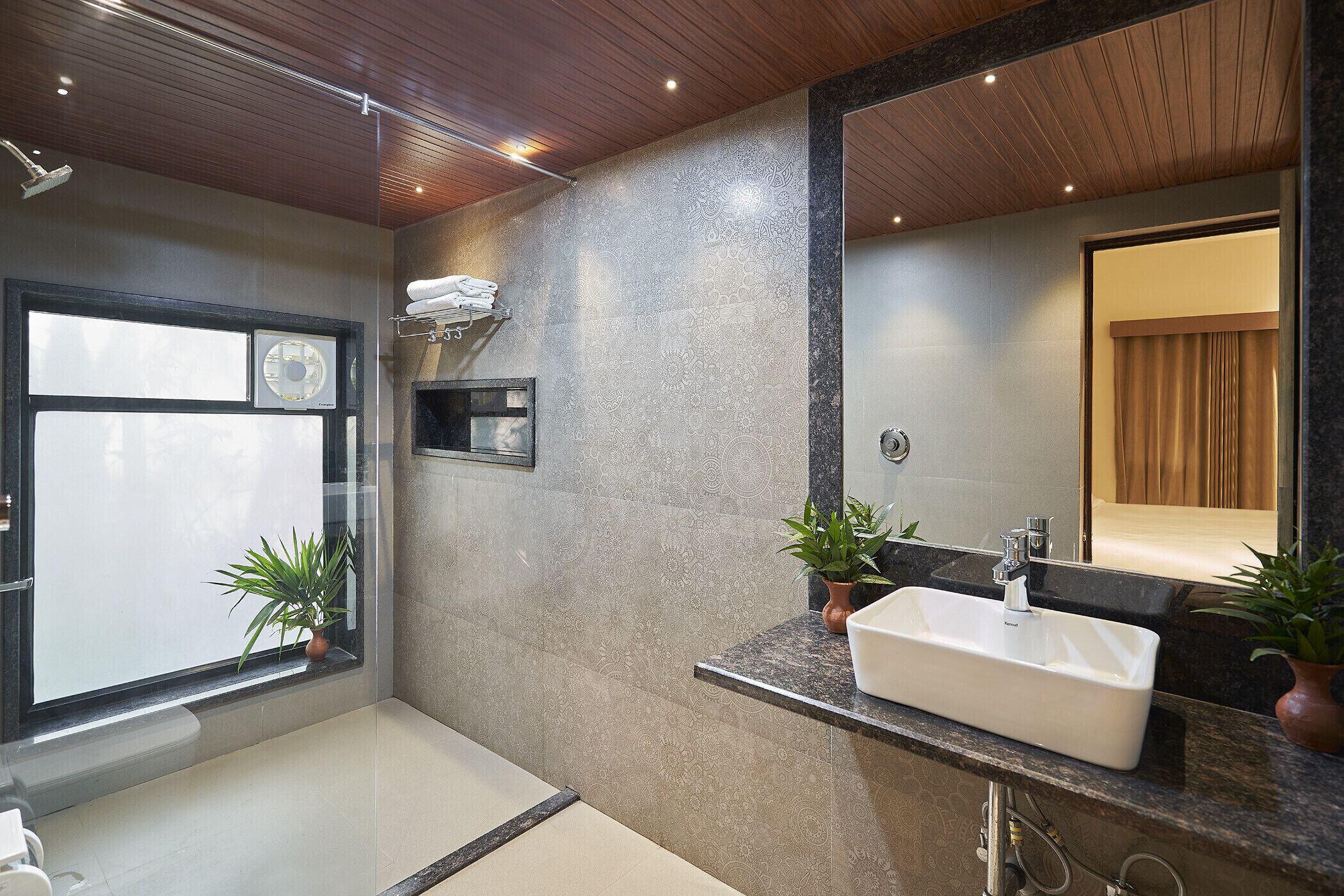 A modern bathroom with a large mirror, a sink, and two potted plants.