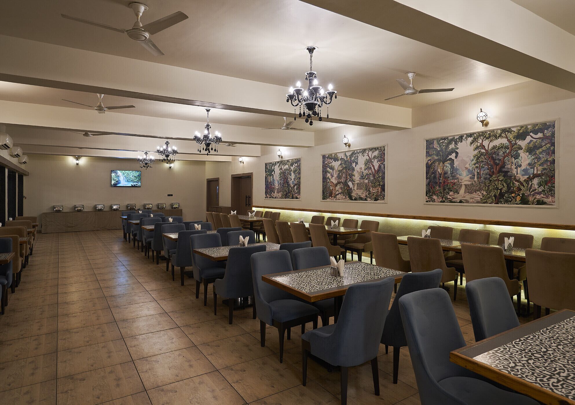 A spacious dining area with multiple tables and chairs, ceiling fans, and wall-mounted chandeliers.
