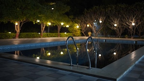 A nighttime swimming pool with metal railings, surrounded by trees and illuminated by string lights. - Olive Resorts & Villas (Kurai)