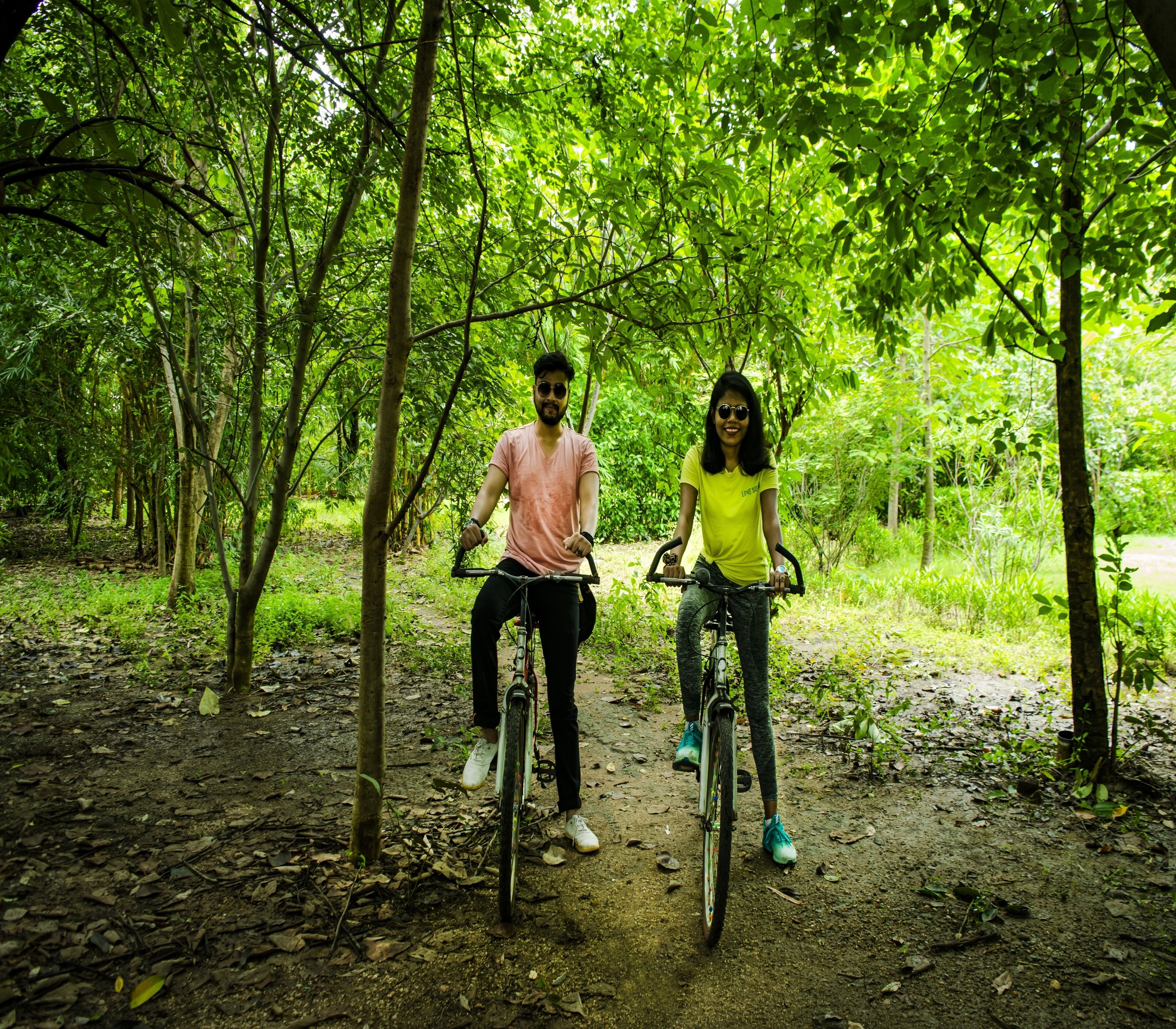 Dos personas en bicicleta por un sendero rural en un área boscosa.