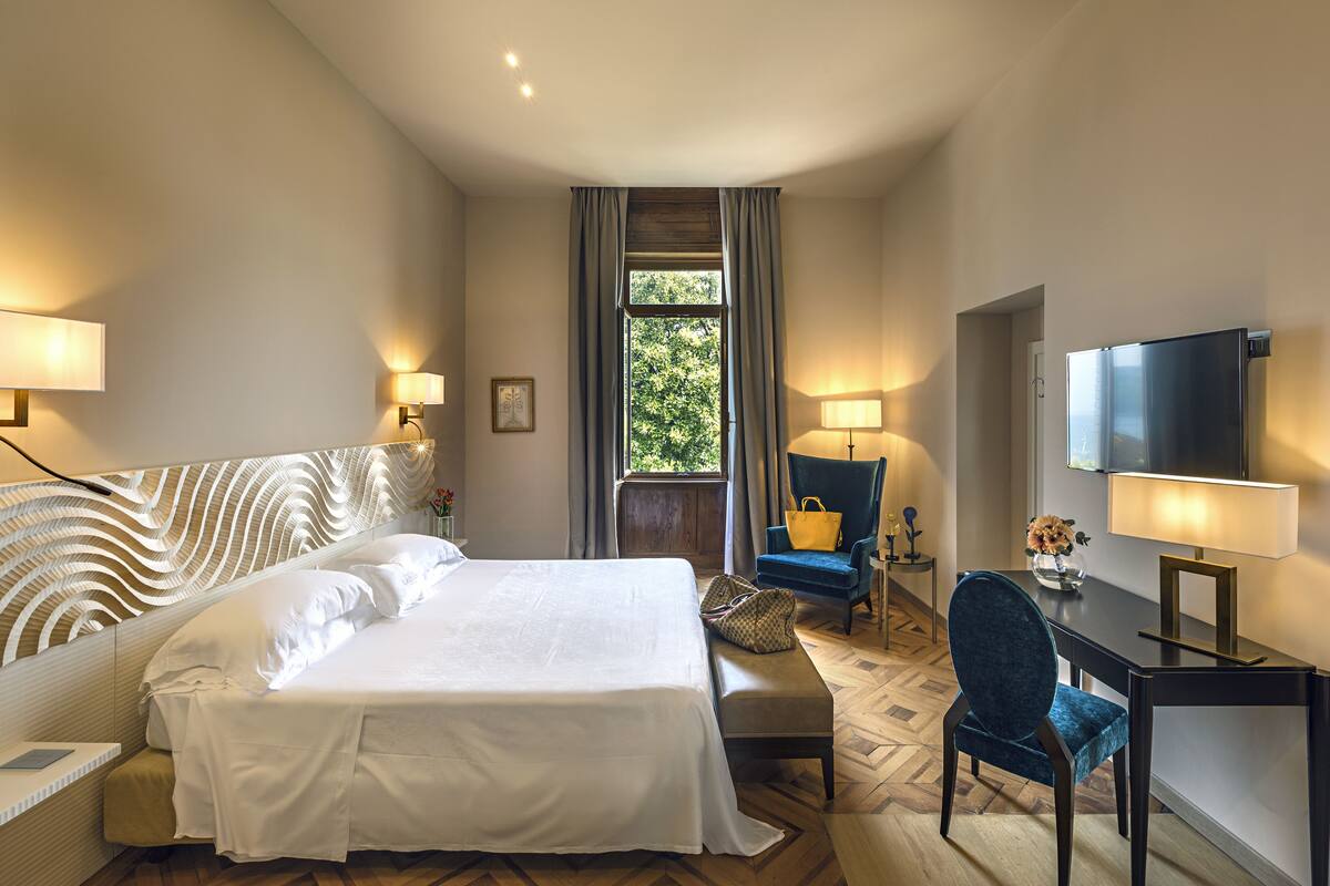 A hotel room with a large bed, a desk, a chair, a television, and a window with curtains.
