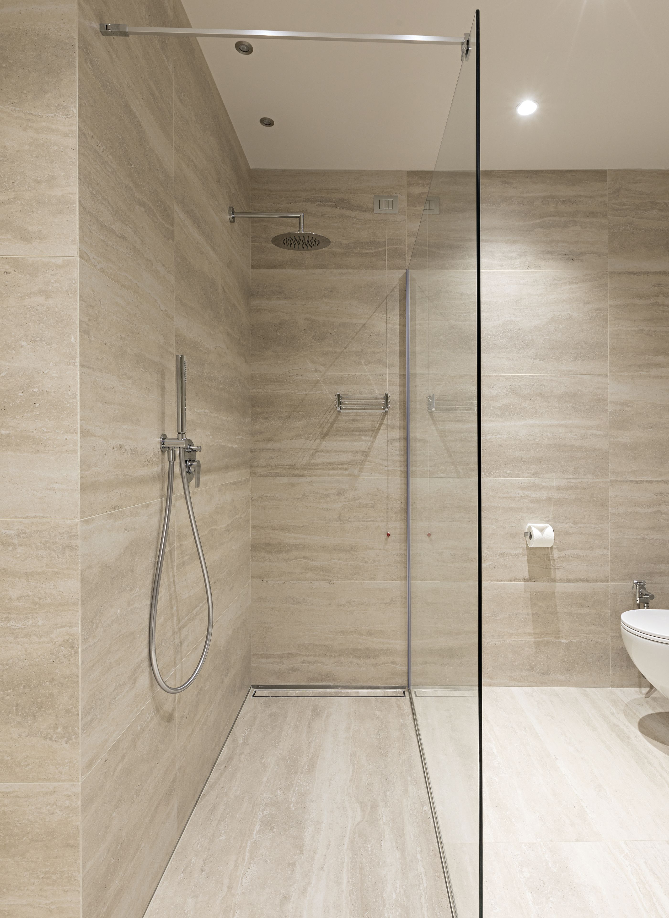 Une salle de bain moderne dotée d’une douche à parois de verre, d’un pommeau de douche à main, d’un robinet mural et d’un porte-rouleau de papier toilette.