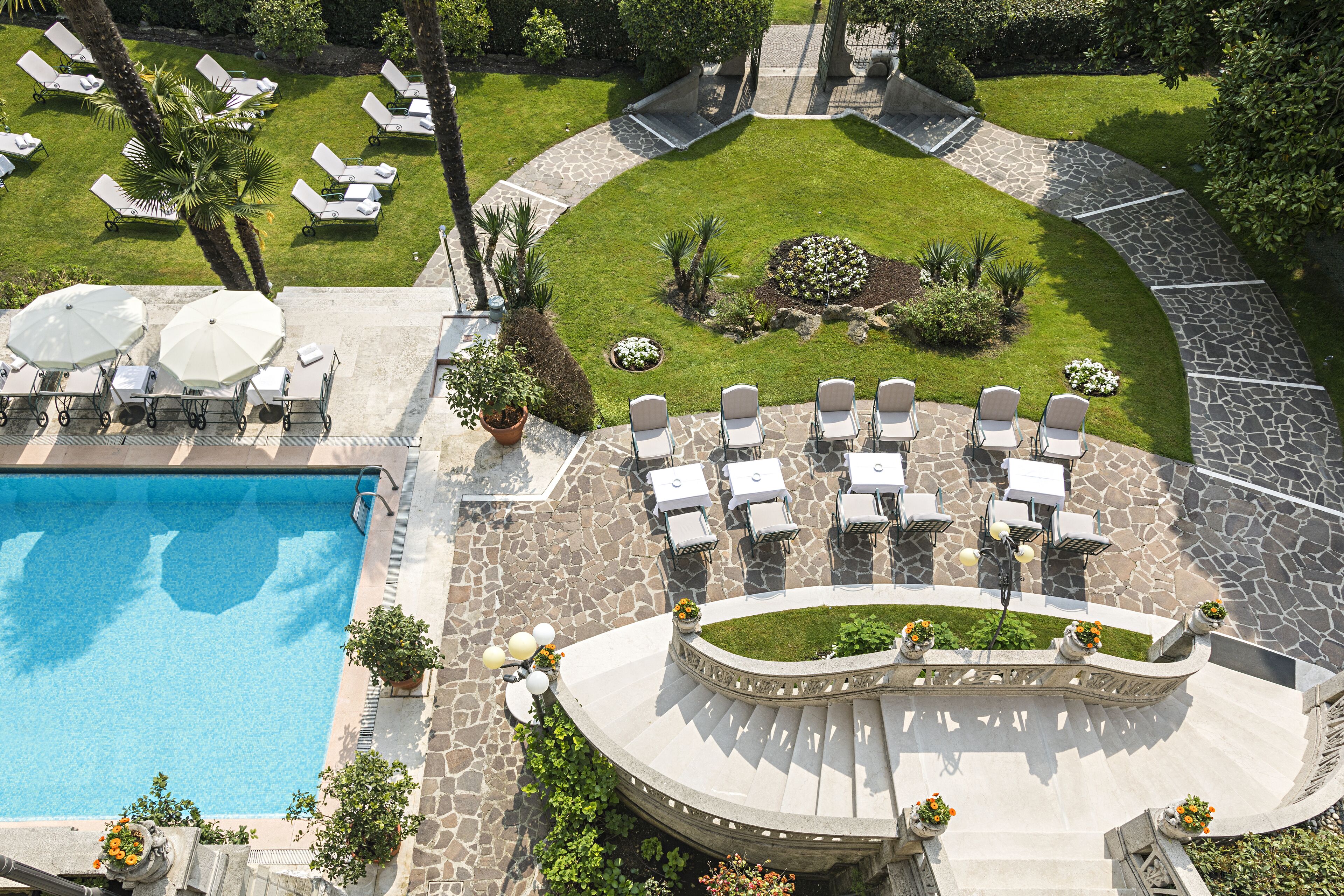A pool area with lounge chairs and umbrellas, surrounded by a stone deck and a well-manicured lawn.