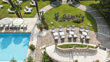 A pool area with lounge chairs and umbrellas, surrounded by a stone deck and a well-manicured lawn.