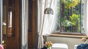 Een kamer met een groot raam, een rode stoel, een witte bank, een glazen bijzettafeltje en een klein tafeltje met een bloemenvaas.
