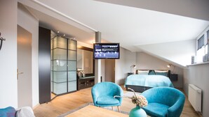 Ein modernes Hotelzimmer mit einem großen Bett, zwei blauen Sessel, einem Holztisch und einem flachbildfernseher an der Wand.