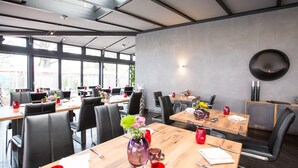 Ein moderner Essbereich mit mehreren Tischen und Stühlen, großen Fenstern und einem zeitgemäßen Interieur.