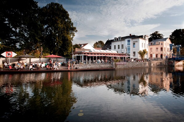 A riverside hotel with outdoor seating, a covered area, and a view of the river. - Hotel und Restaurant Fackelgarten (Plau am See)