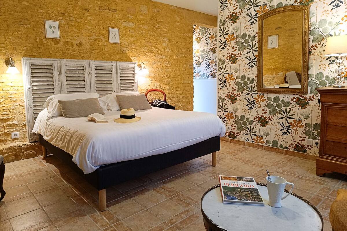 A bedroom with a bed, a round table with a book and a mug, a dresser, and a mirror.