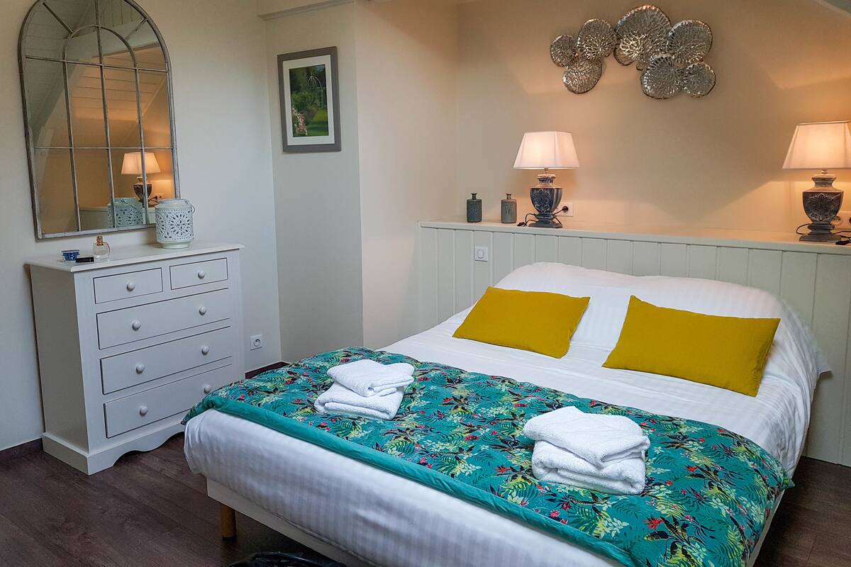 A neatly arranged bedroom with a bed, a dresser, a mirror, and wall decor.