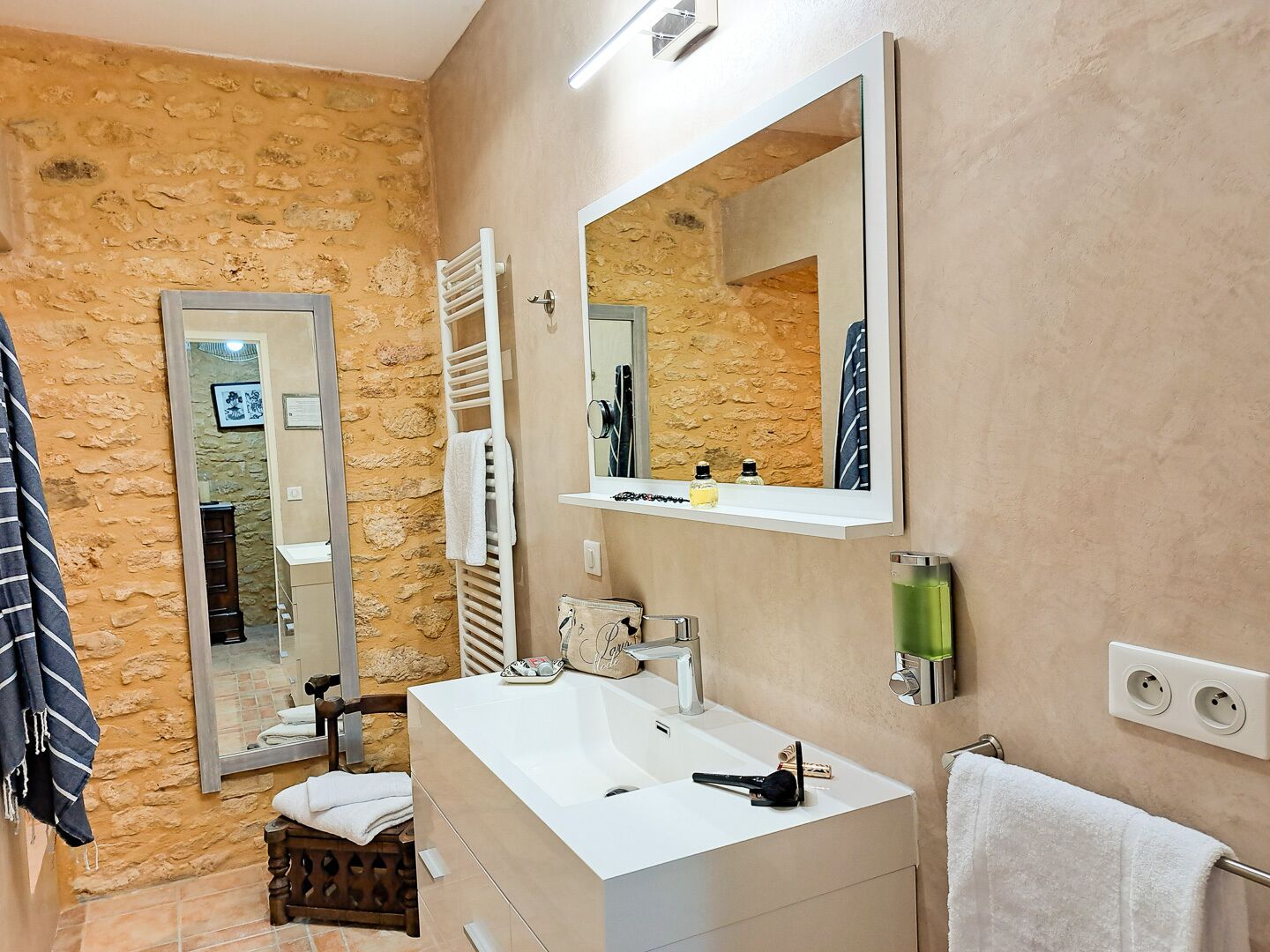 A bathroom with a stone wall, a white sink, a mirror, and a towel rack.