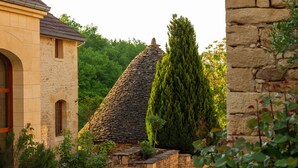 A stone building with a thatched roof, surrounded by greenery and a tall coniferous tree. - Aux Bories de Marquay (Marquay)