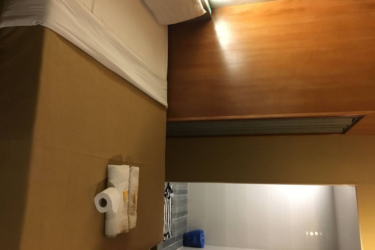 A bathroom with a wooden ceiling, a towel rack with towels, a toilet paper holder, and a blue trash bin.