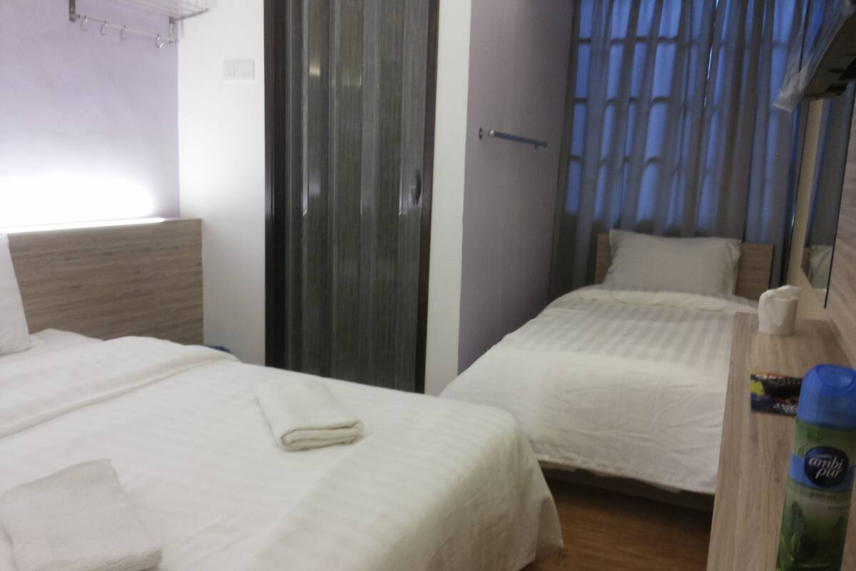 A hotel room with two beds, a wooden headboard, a window with curtains, and a wooden dresser with a bottle on it.