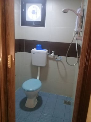 A small bathroom with a toilet, a shower, and a wall-mounted light fixture. - Suria Cameron Hotel (Tanah Rata)