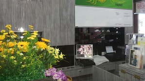 Balcão de recepção com uma placa verde para o Hotel Suria, um relógio e um arranjo floral.
