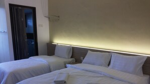 Quarto de hotel com duas camas, cada uma com roupa de cama e almofadas brancas, e cabeceira com iluminação embutida.