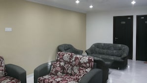 Uma área de espera com dois sofás e uma poltrona, teto com iluminação embutida e duas portas ao fundo.