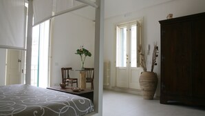 A bedroom with a bed, a wooden cabinet, and a dining area with chairs and a vase of flowers. - Le Tre Vie Apartment & Room (Matera)
