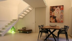 A dining area with a wooden table and four chairs, a staircase, and a wall-mounted abstract painting. - Le Tre Vie Apartment & Room (Matera)