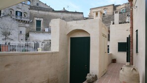 A narrow alleyway with a green door, a large terracotta pot, and a tiled floor. - Le Tre Vie Apartment & Room (Matera)