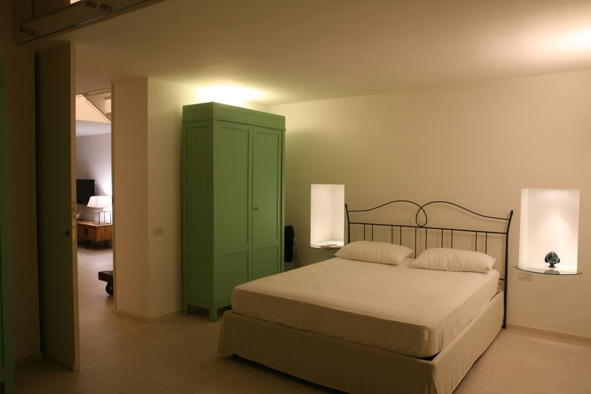 A bedroom with a bed, a green wardrobe, and bedside lamps.