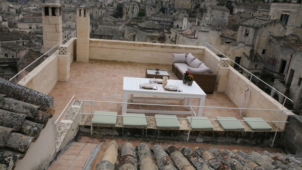 A rooftop terrace with a white table set for dining, a sofa, and several chairs. The terrace overlooks a densely packed urban area with historic buildings. - Le Tre Vie Apartment & Room (Matera)