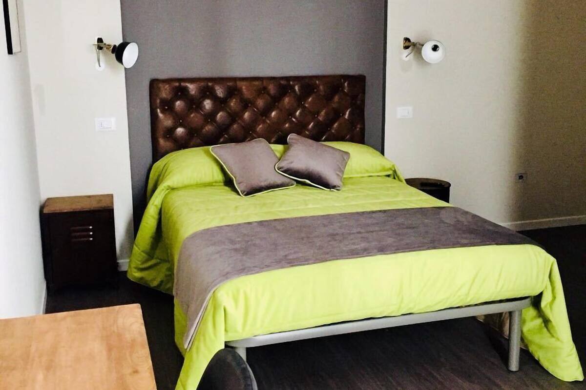 A single bed with a tufted headboard, green bedding, and two pillows.