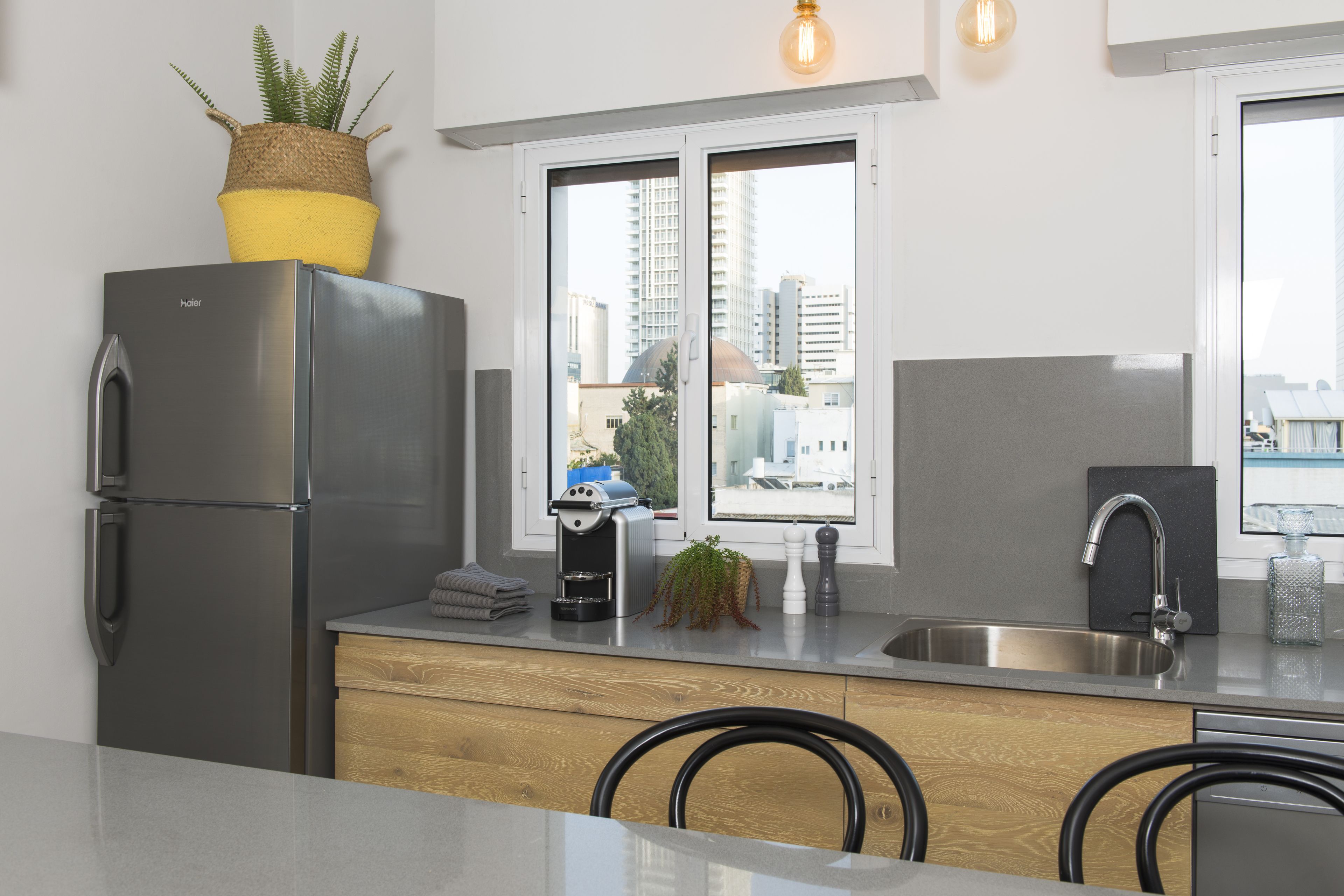 A modern kitchen with a stainless steel refrigerator, a coffee machine, and a window with a city view.