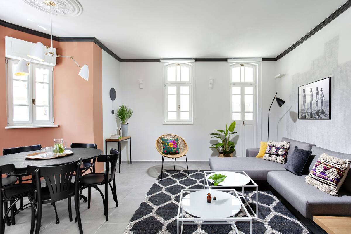 Ein modernes Wohnzimmer mit einem runden Esstisch, schwarzen Stühlen, einem grauen Sofa und einem schwarz-weißen Teppich.