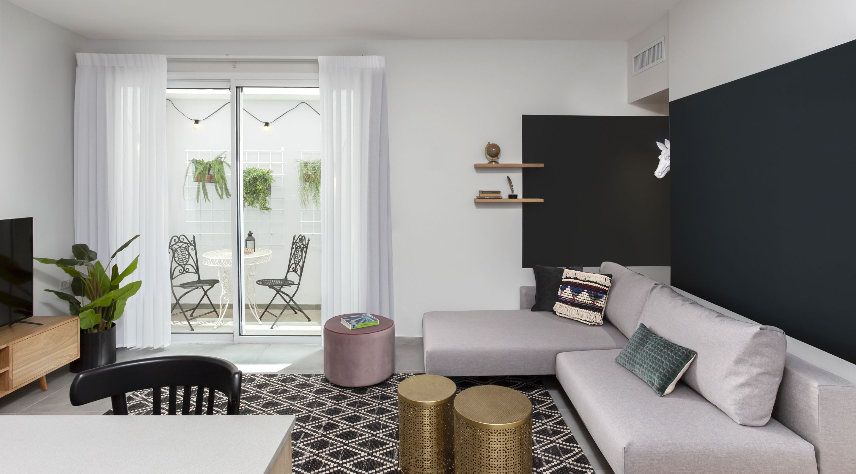 Una sala de estar moderna con un sofá gris, una mesita redonda pequeña, un televisor y un balcón con plantas.
