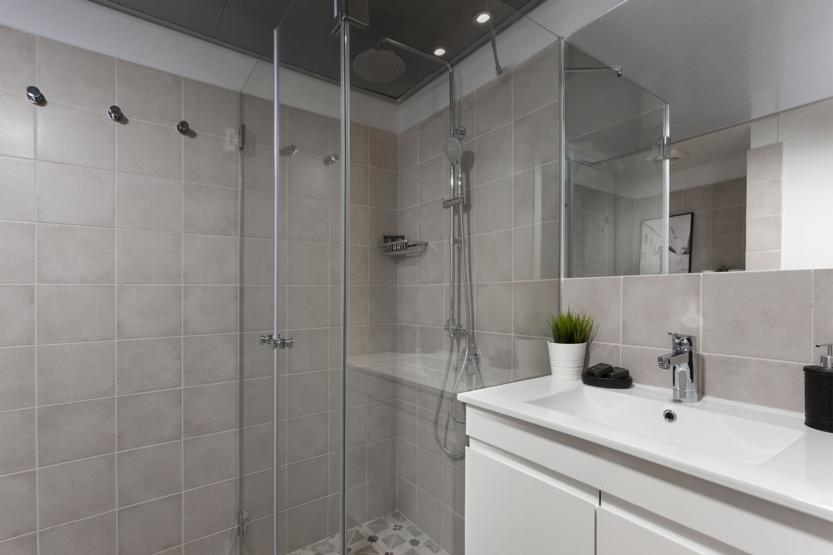Een moderne badkamer met een glazen douchecabine, een witte wastafel en een spiegel.