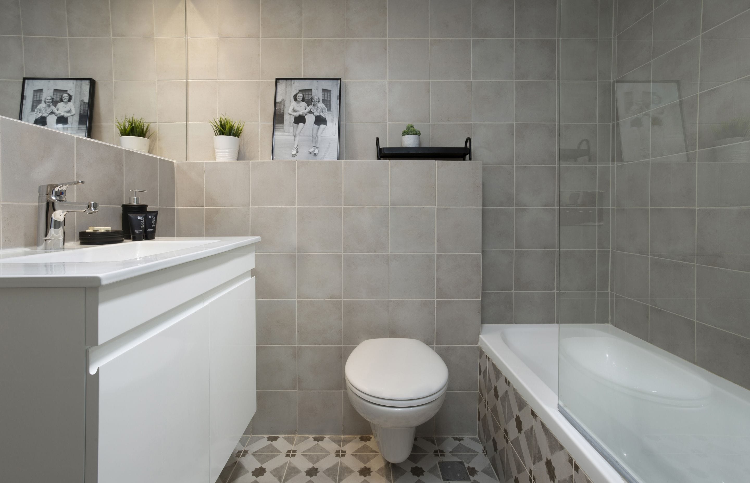 A bathroom with a toilet, sink, and bathtub. There are two potted plants on the wall above the toilet.