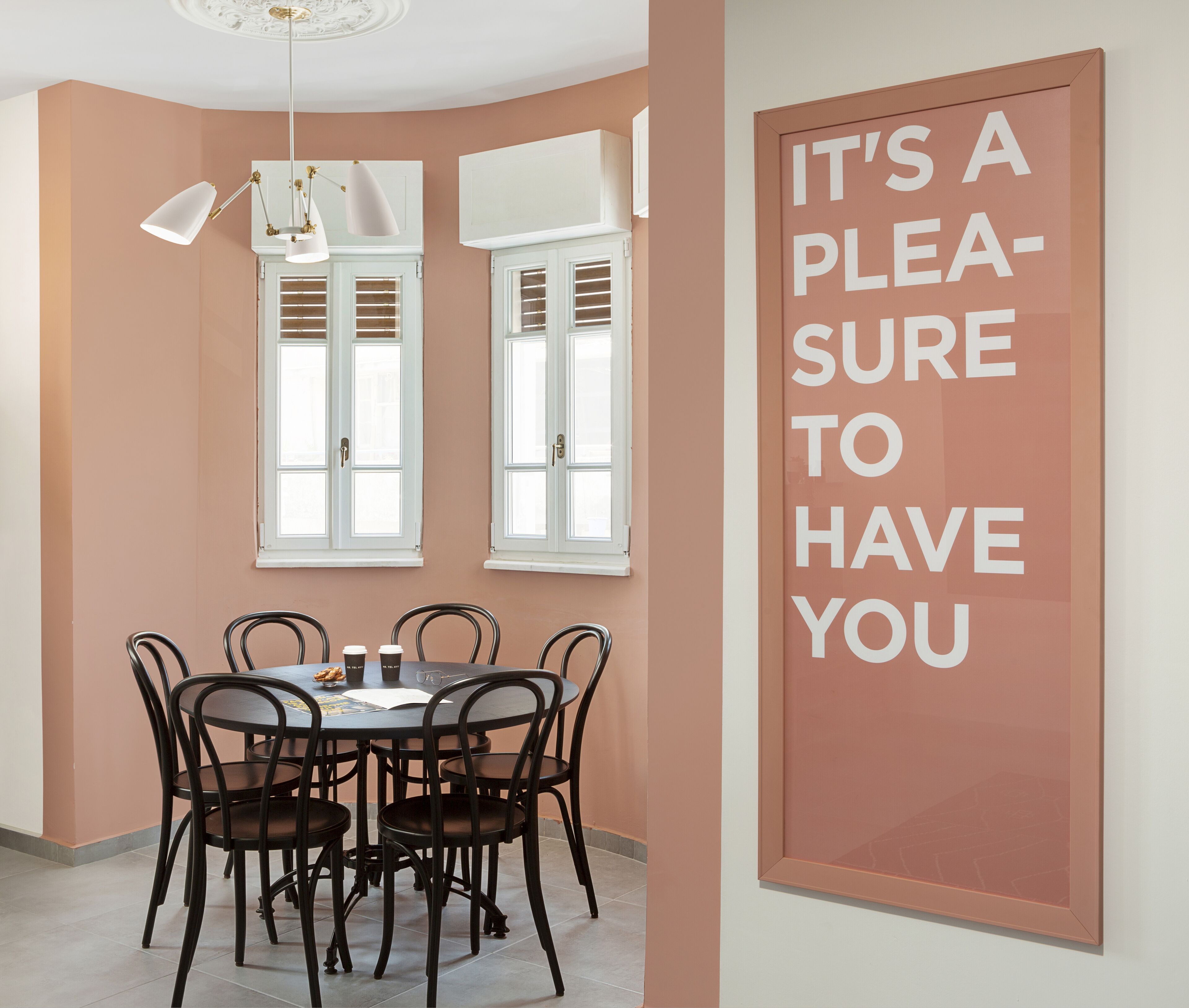 A dining area with a round table, black chairs, and a wall-mounted sign that reads "IT'S A PLEASURE TO HAVE YOU".