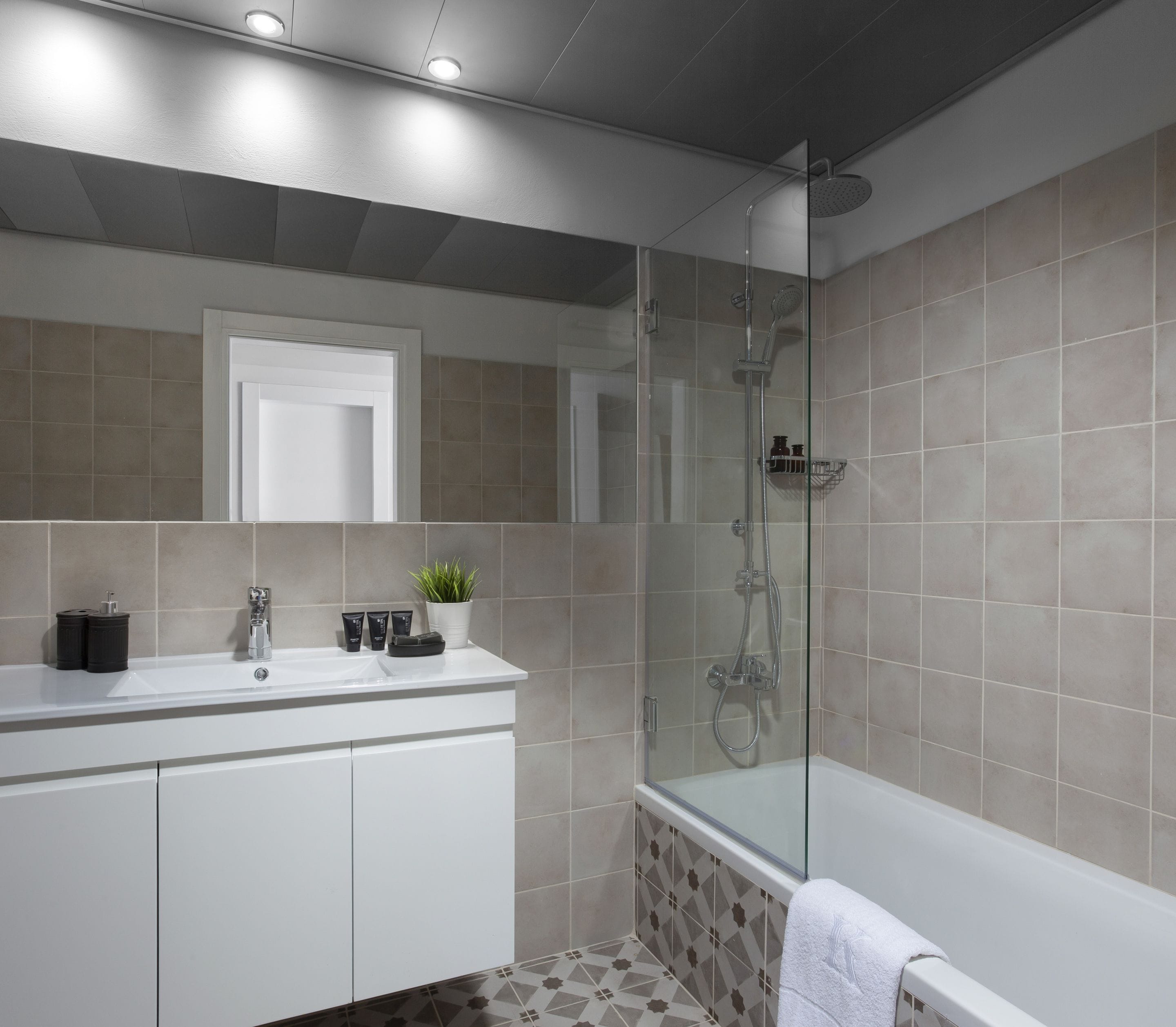 A modern bathroom with a glass-enclosed shower, a white vanity with toiletries, and a patterned floor.