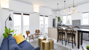 A modern living room with a sofa, chairs, a coffee table, and a kitchen area with bar stools and pendant lights. - Mr. Katinsky - By TLV2GO (Tel Aviv)