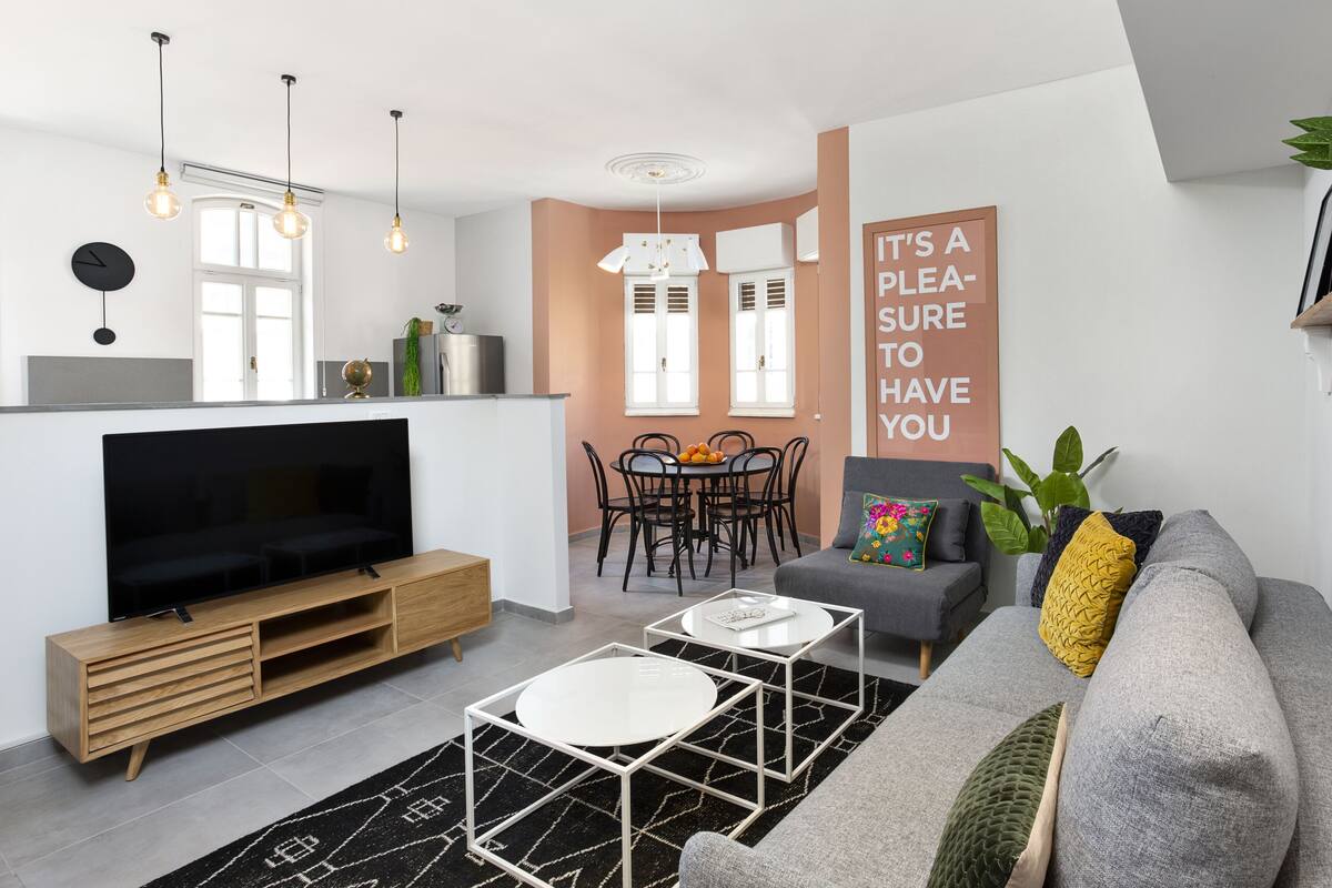 Ein modernes Wohnzimmer mit Flachbildfernseher, grauem Sofa, Couchtisch und Essbereich mit Tisch und Stühlen.