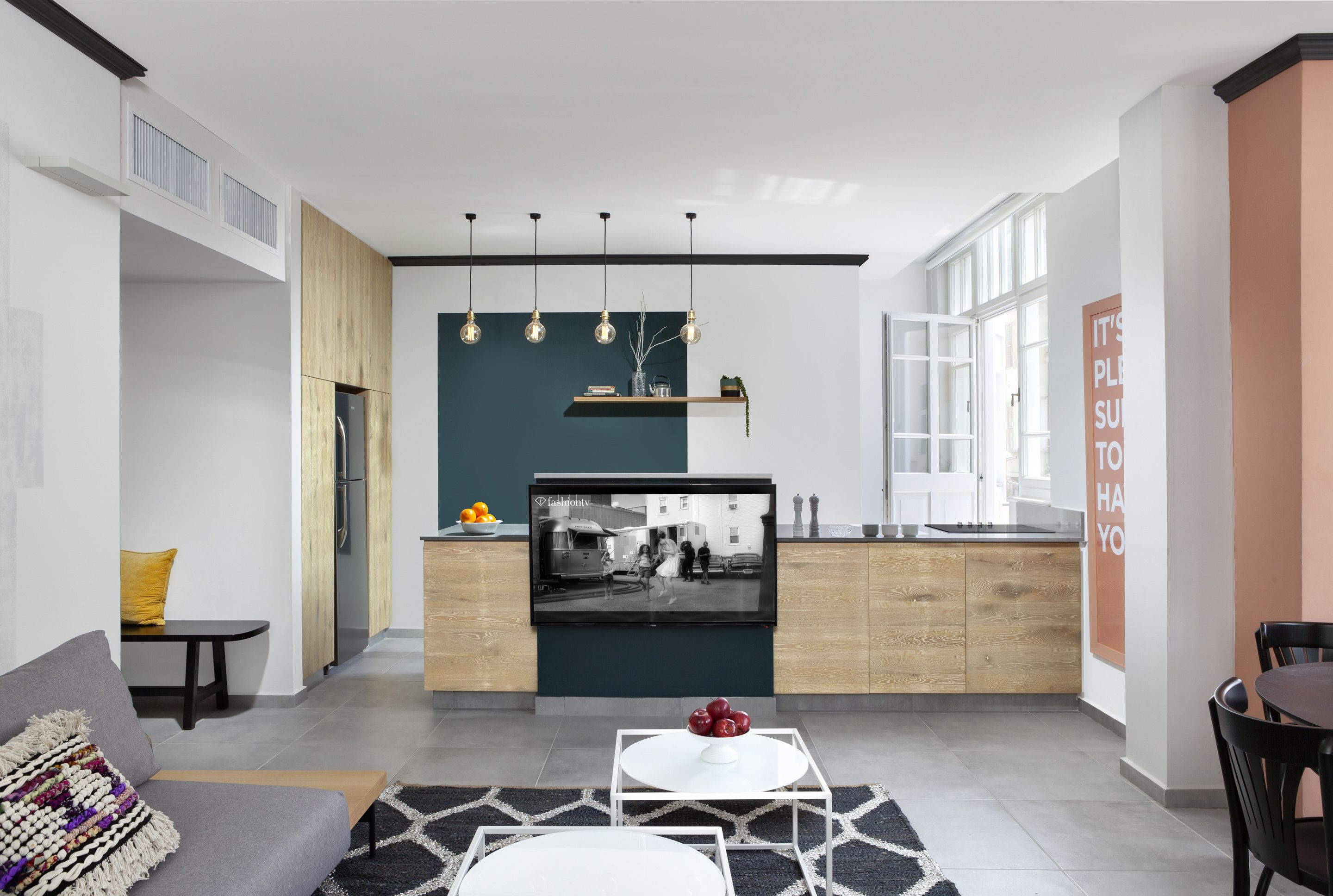 A modern kitchen with a built-in TV, wooden cabinets, and pendant lighting.
