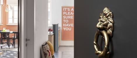 Un interior moderno con una escultura de metal decorativa en una pared oscura, un banco con cojines y un cartel con texto.