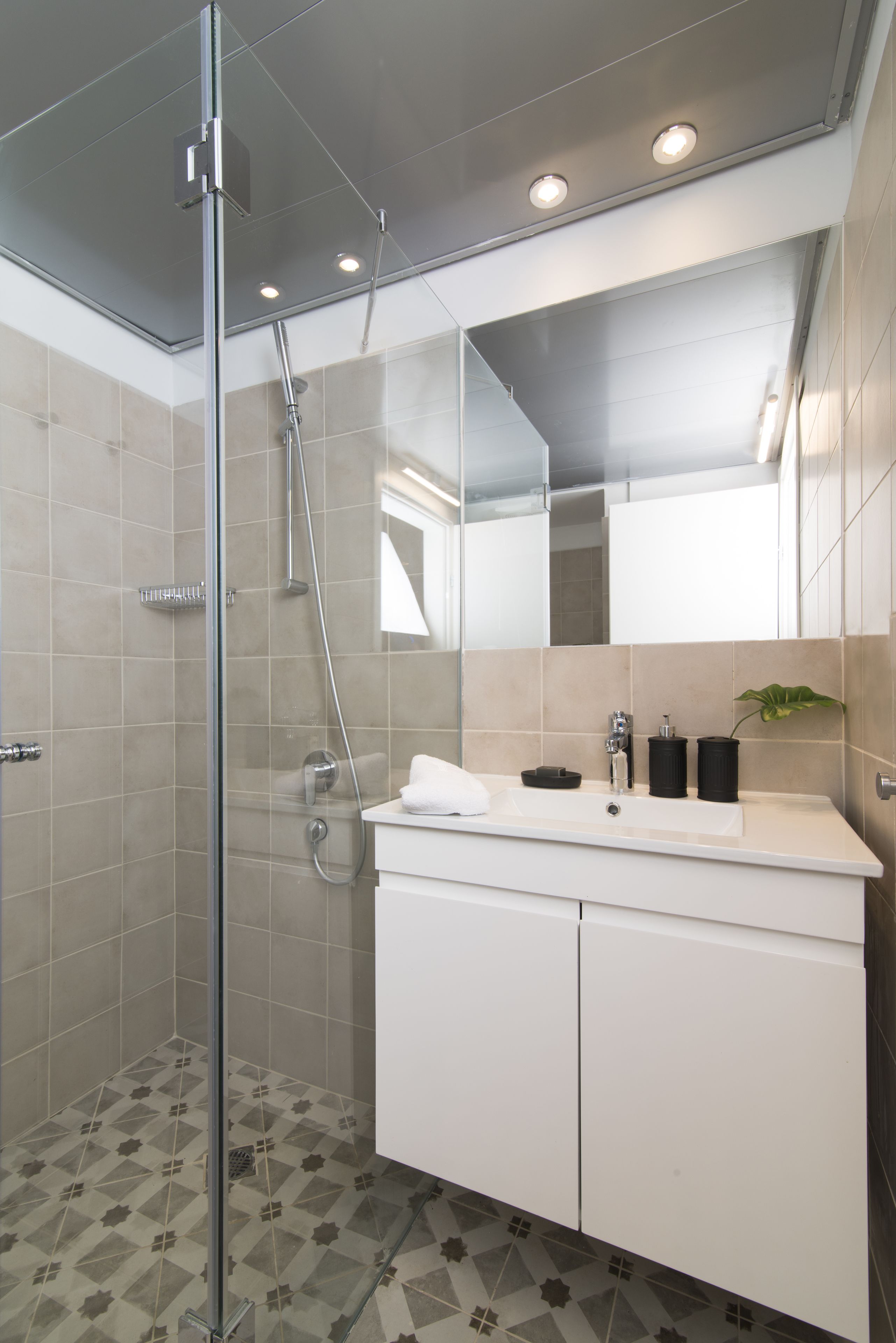 A modern bathroom with a glass-enclosed shower, a white vanity with black soap dispensers, and a large mirror above the sink.