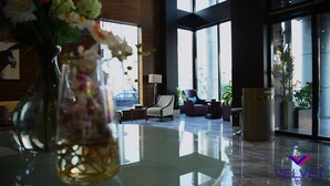 A modern hotel lobby with a glass table, a vase with flowers, a patterned armchair, and a reception desk.