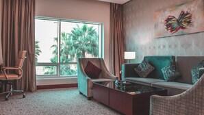 A hotel room with a large window, a sofa, a chair, a coffee table, and a wall with a butterfly painting.