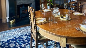Une salle à manger avec une table ronde en bois, dressée pour six personnes, une cheminée et un lustre.
