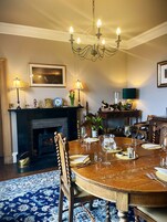A dining room with a round wooden table set for six, a fireplace, and a chandelier.