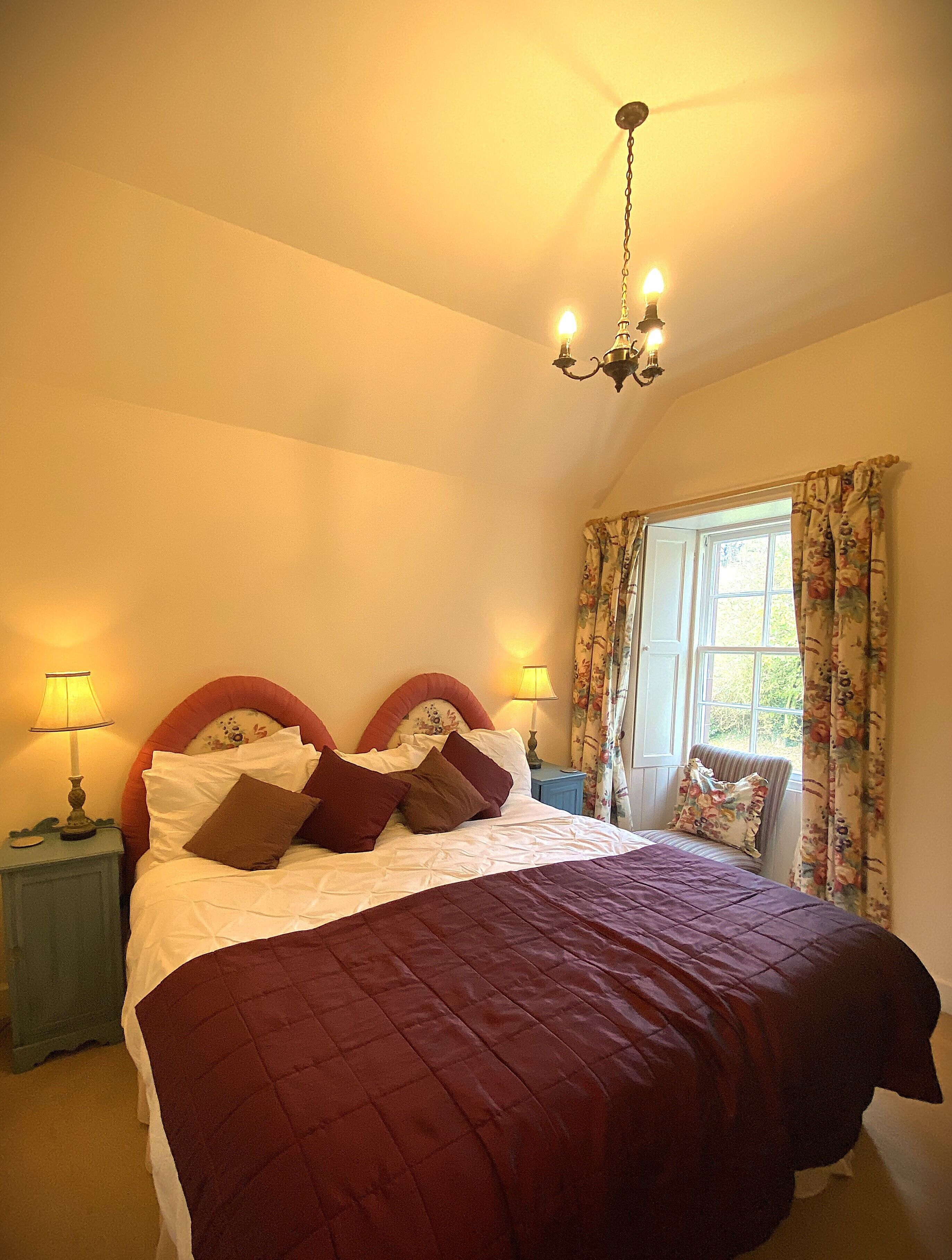 A bedroom with a large bed, two bedside lamps, a floral curtain, and a chandelier.