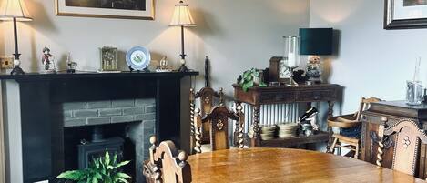 A dining room with a large wooden table, chairs, a chandelier, a fireplace, and framed artwork on the walls.