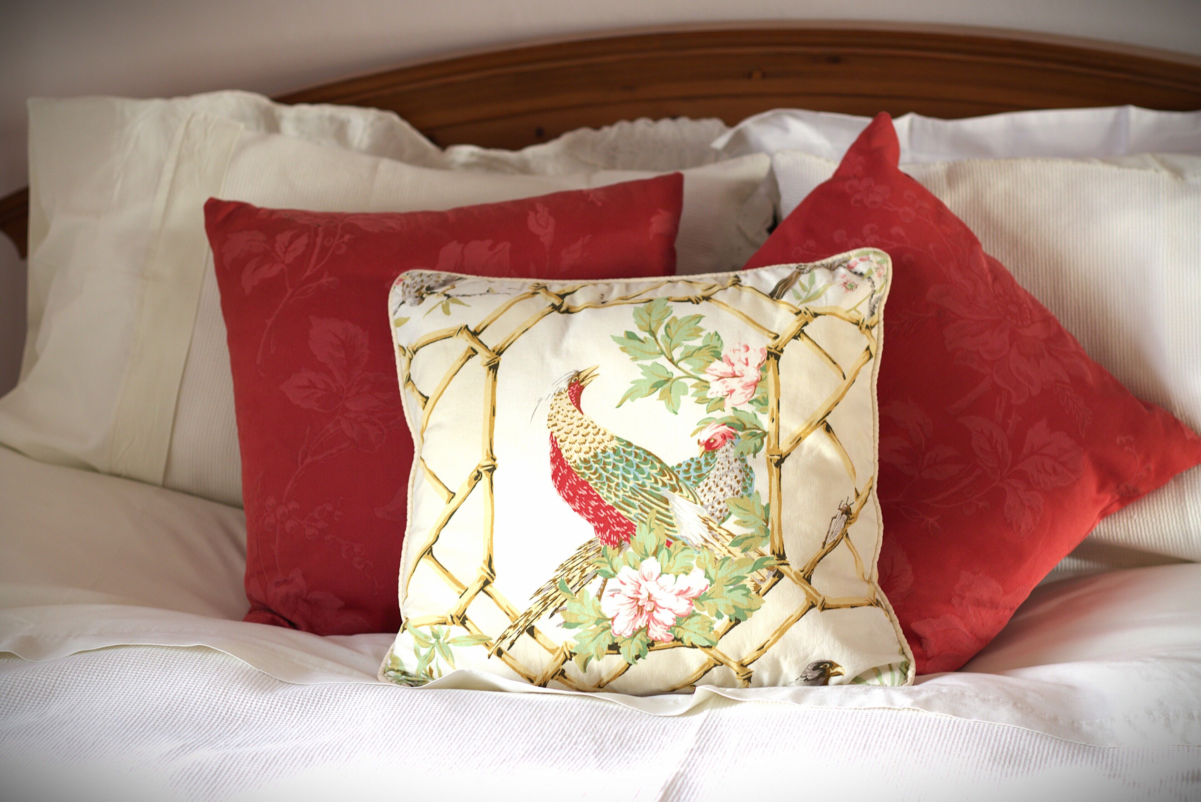 A bed with white bedding and red pillows, one with a bird design.