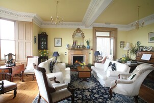 A traditional living room with a fireplace, white furniture, and a patterned rug.